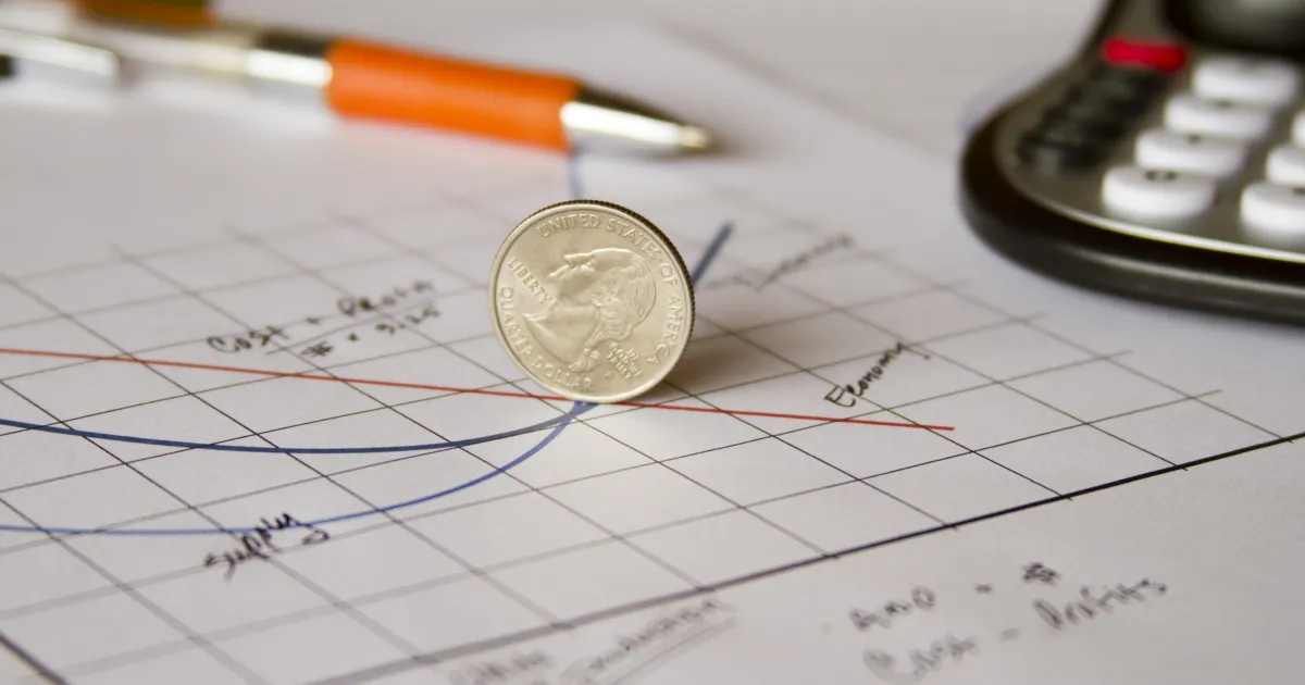 A coin on a table on top of a graph showing supply and demand.